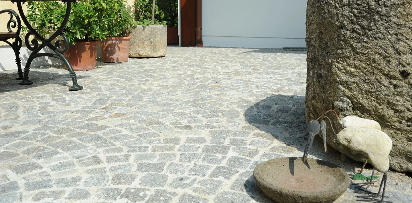 Innenhof mit Granit-Kleinsteinpflaster im Bogenverband, daneben Pflanztröge und ein alter Mauerstein