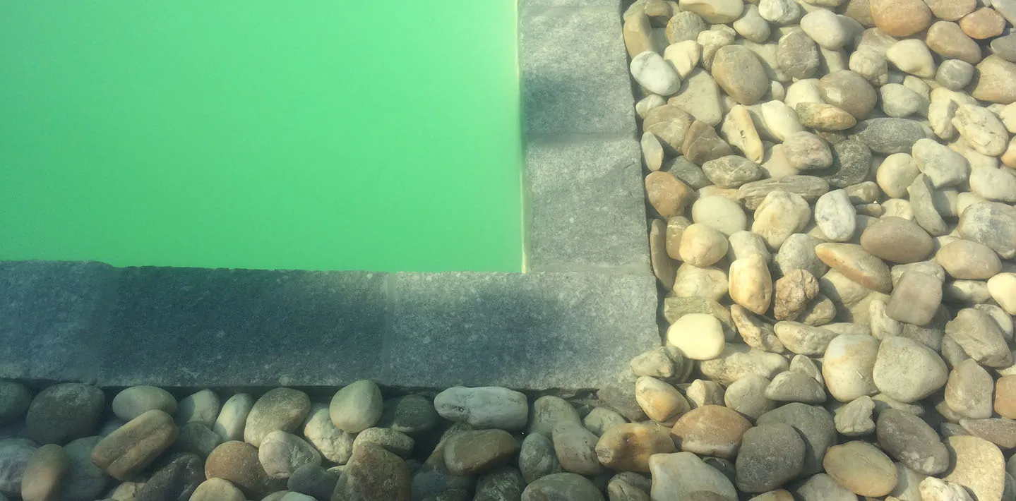 Poolrand mit Granit-Randsteinen, dahinter ein Streifen aus gewaschenen Flusskieseln als Sickerfläche