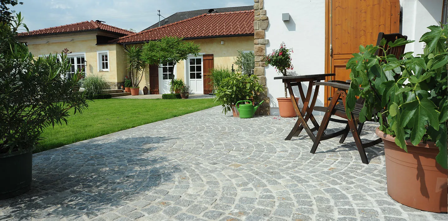 Terrasse aus Granit-Kleinstein im Segmentbogen, verlegt neben Rasen und Hausmauer