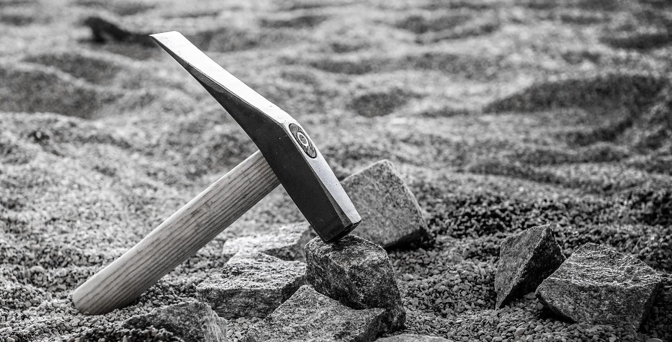 Pflasterhammer, aufgestellt auf gebrochenen Granitsteinen im Splittbett, Schwarzweißaufnahme